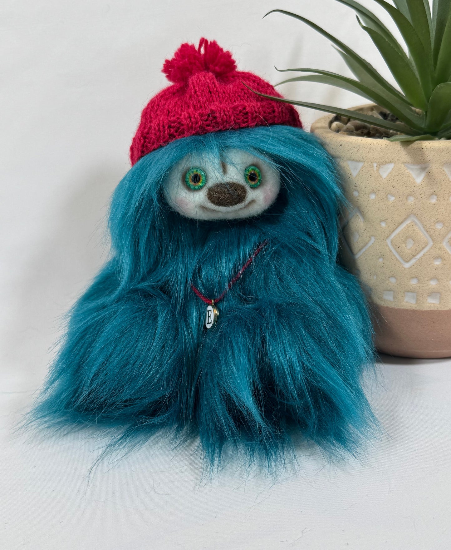 Frimousse Edelis 17 cm en fausse fourrure vert sarcelle avec bonnet rouge tricoté main et pendentif initial