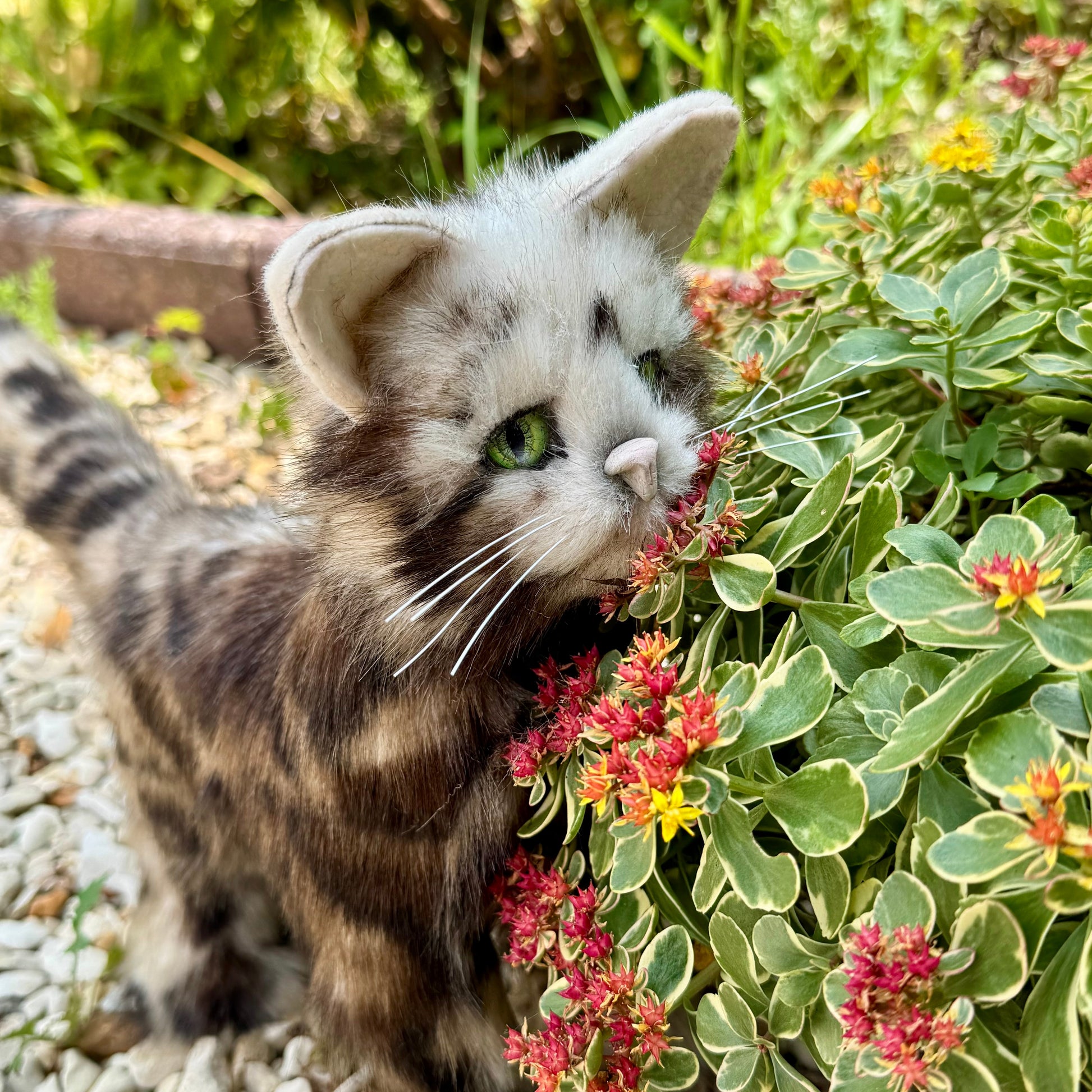 Chat en peluche réaliste de collection Topaze dans un jardin fleuri