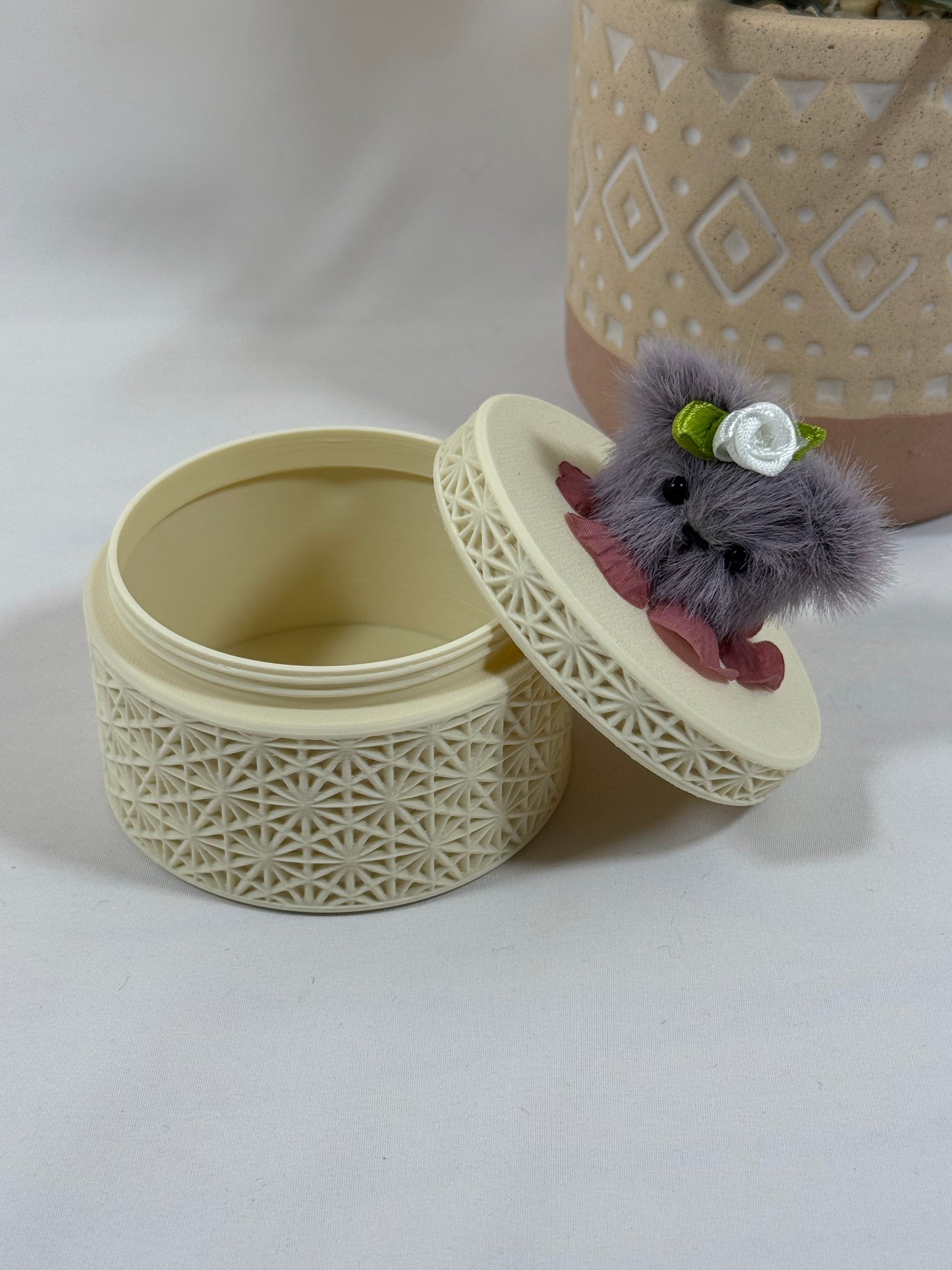 Boîte ronde crème à motif géométrique avec tête d'ours mauve foncé cousue à la main sur le couvercle.