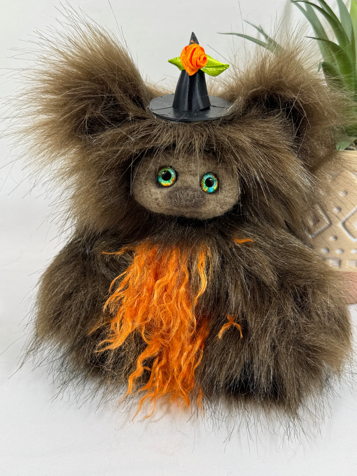 Carabistouille, Frimousse Halloween artisanale de 16 cm en fausse fourrure brune et orange, avec yeux multicolores et chapeau de sorcière noir.