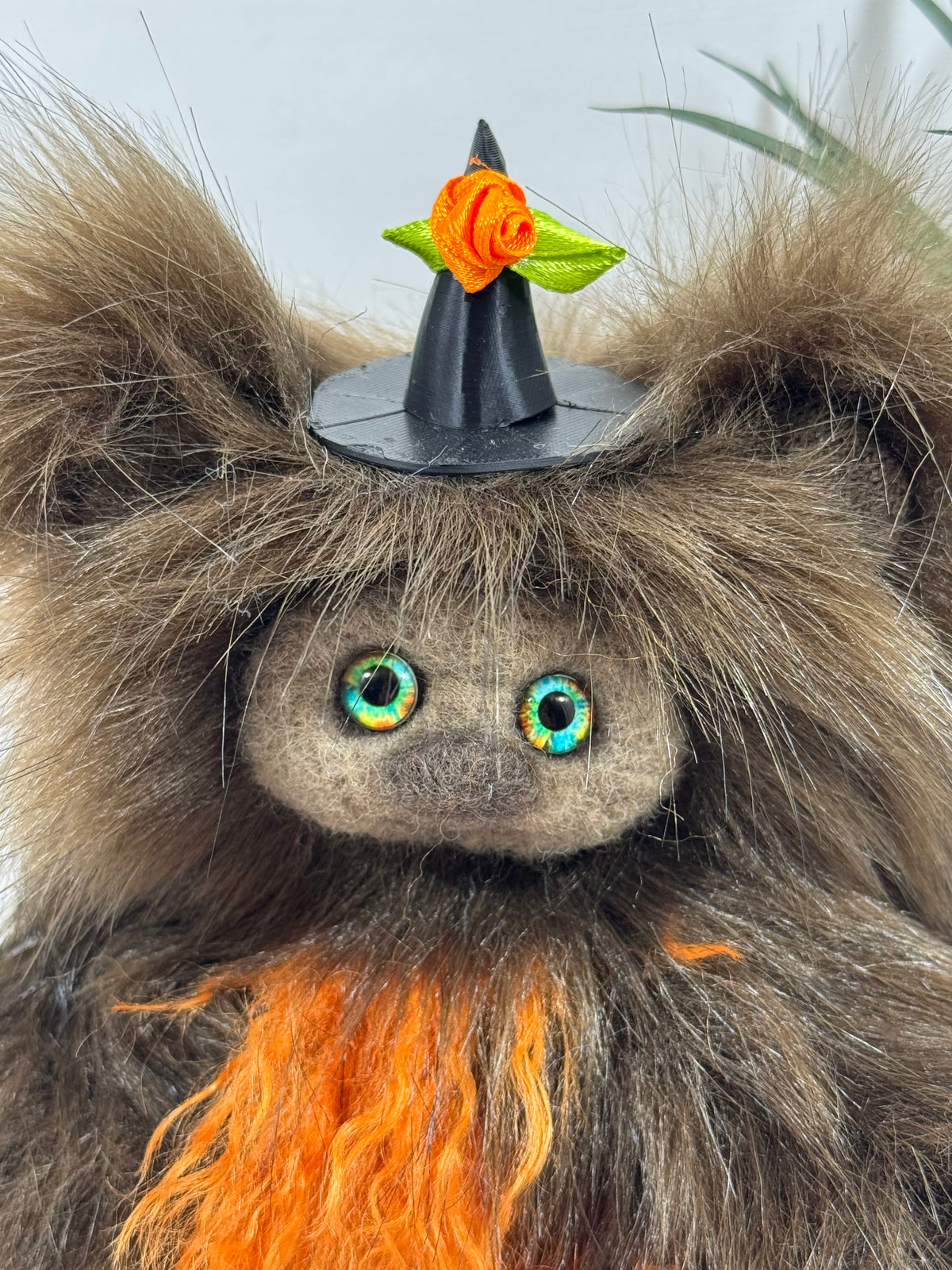 Frimousse de collection Carabistouille, petite créature d’Halloween de 16 cm faite main, au pelage brun ébouriffé, ventre orange flamboyant et chapeau de sorcière décoré d’une rose orange.