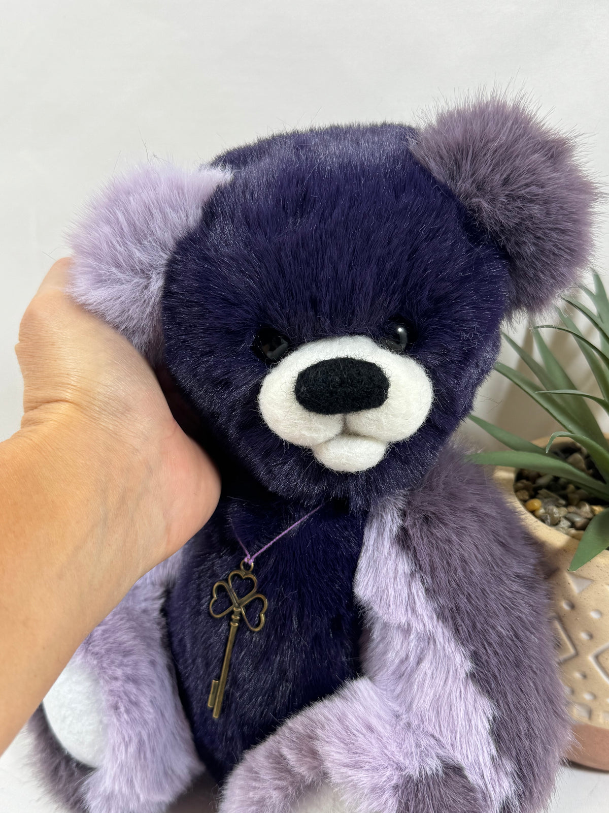 Détail du visage de Myrtille, ours artisanal violet avec museau blanc en feutrine, yeux noirs et oreilles lilas duveteuses.