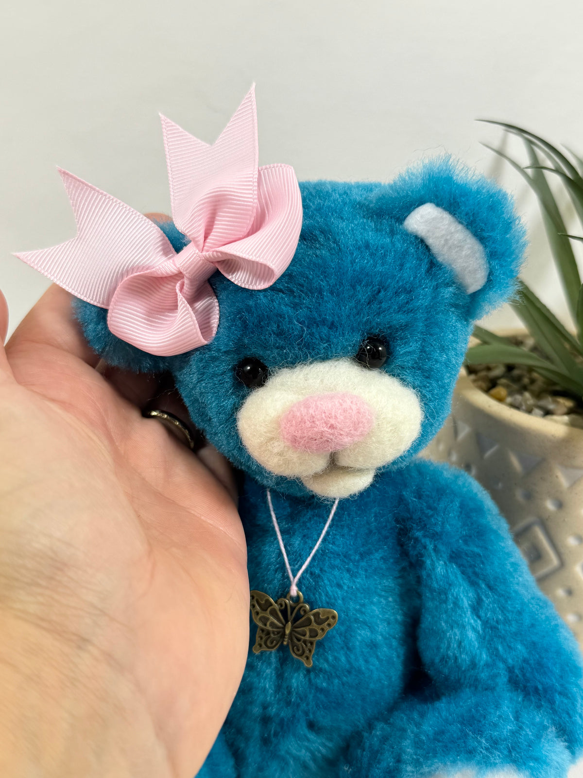 Gros plan sur Papillotte, oursonne artisanale turquoise avec museau blanc, petit nez rose et grand nœud décoratif rose.