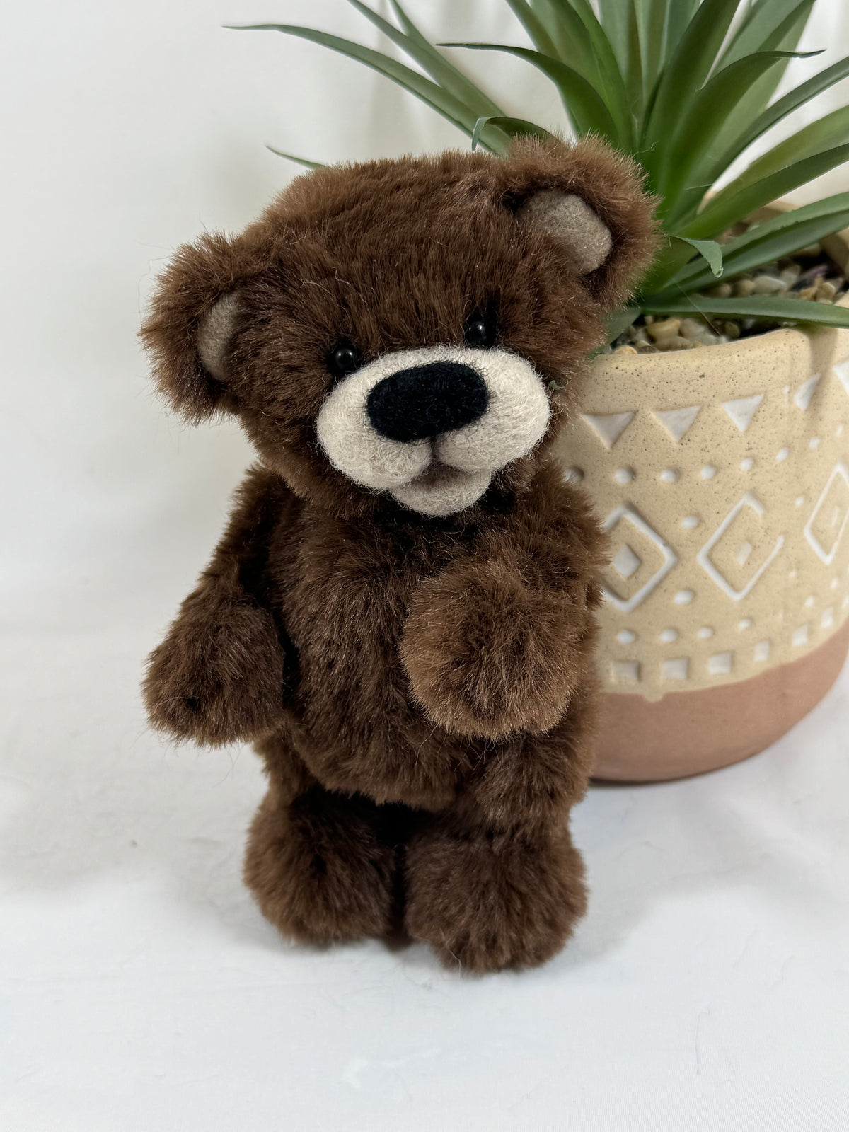 Gros plan sur Chocolou, petit ours de collection marron avec museau crème en feutrine, yeux noirs et oreilles rondes.