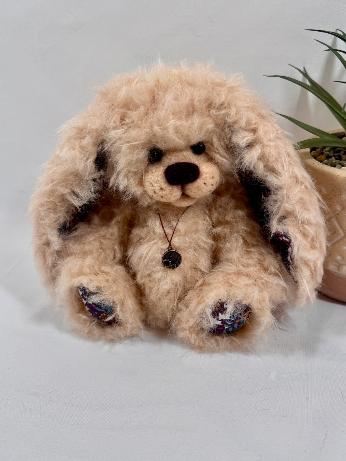 Pomponette, lapin de collection artisanal de 20 cm en fausse fourrure bouclée abricot, avec grandes oreilles tombantes et coussinets fleuris.