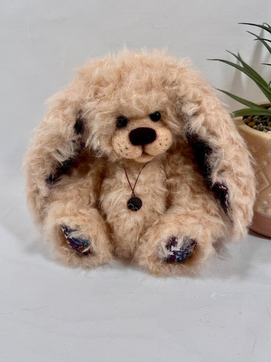 Pomponette, lapin de collection artisanal de 20 cm en fausse fourrure bouclée abricot, avec grandes oreilles tombantes et coussinets fleuris.
