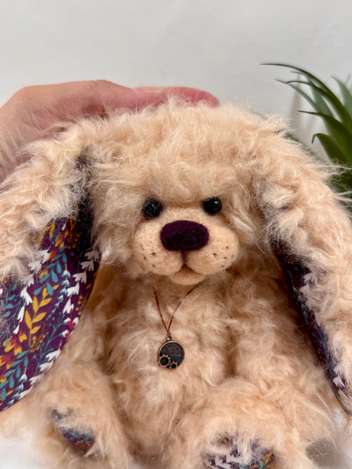 Gros plan sur Pomponette, lapine artisanale aux poils bouclés beige abricot, avec museau en feutrine, yeux noirs et longues oreilles.