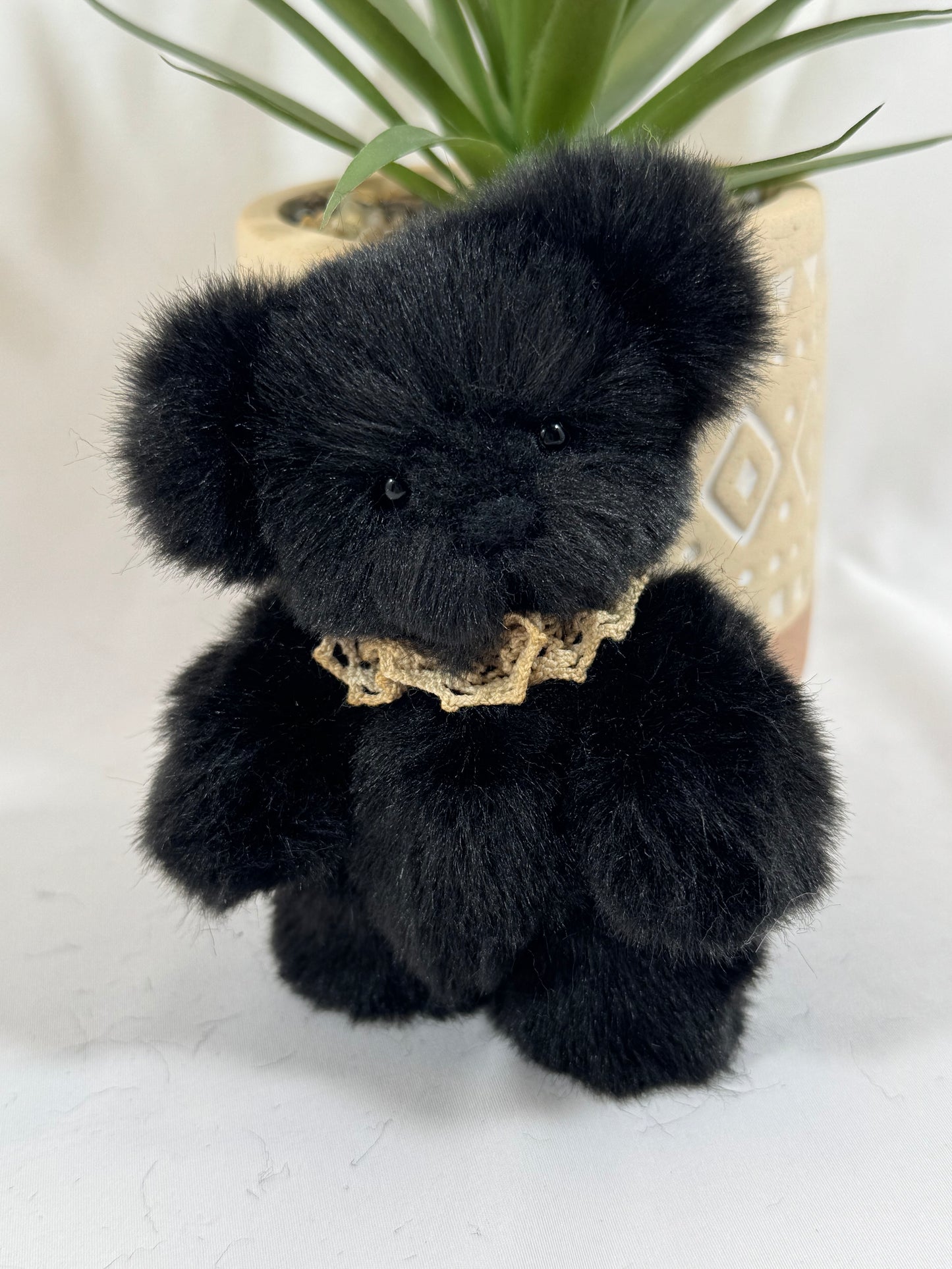 Ours de collection Onyx 10 cm posé près d’une plante, fausse fourrure noire douce