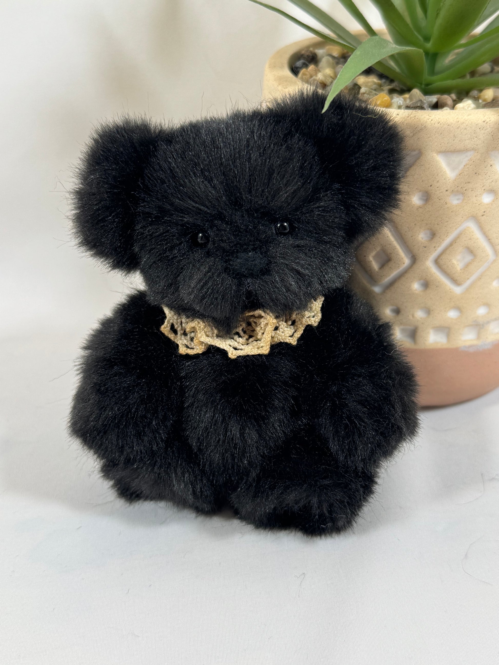 Petit ours noir en fausse fourrure, pièce artisanale Onyx tenue dans une main.